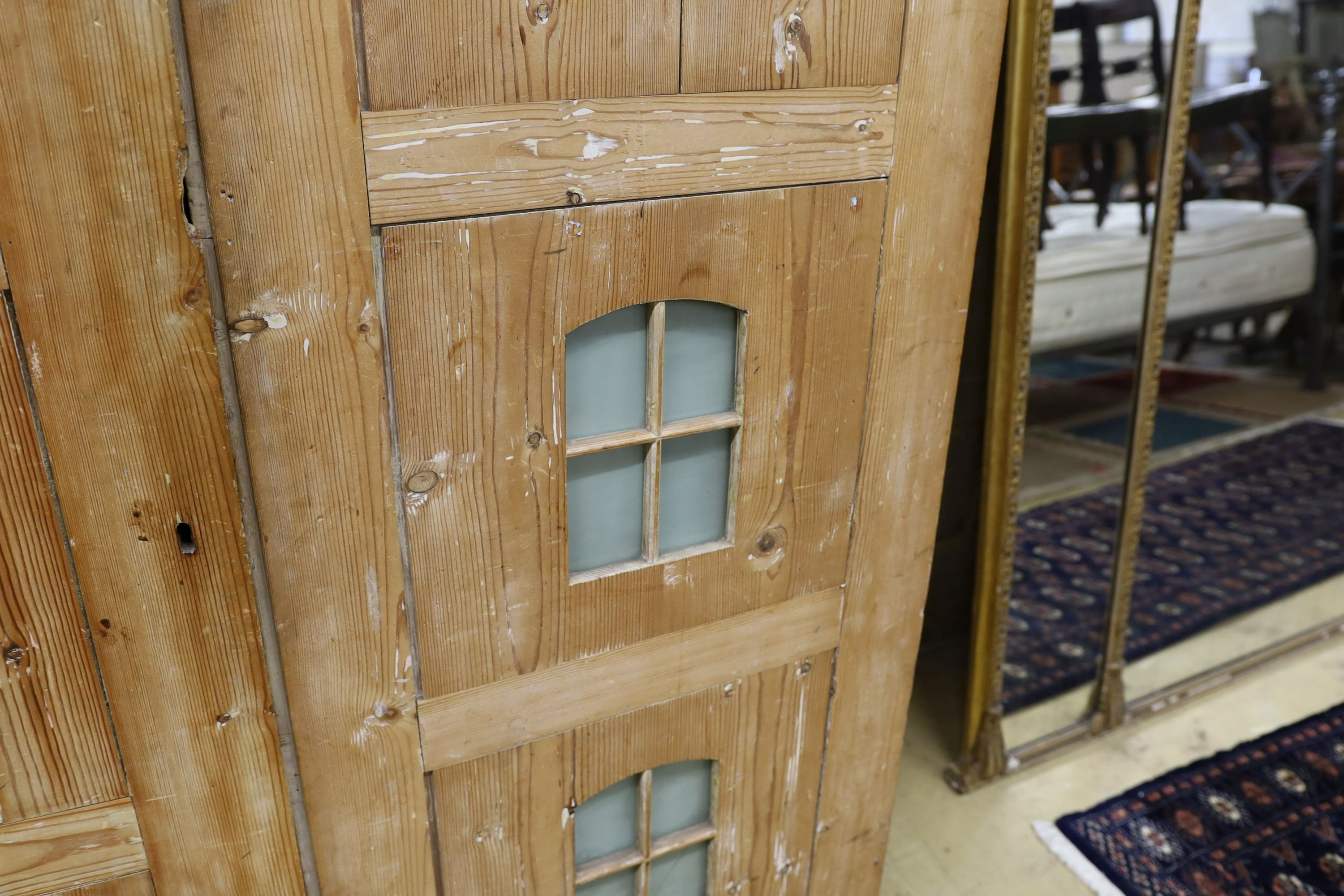 A 19th century stripped pine hall cupboard modelled as a dolls house the two door nine window facade enclosing a compartmented interior, width 182cm, depth 46cm, height 192cm